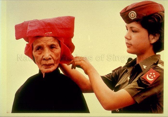 A samsui woman receiving help before heading out for a celebratory march-past at the 1980 National Day Parade. Image courtesy of The National Archives of Singapore.